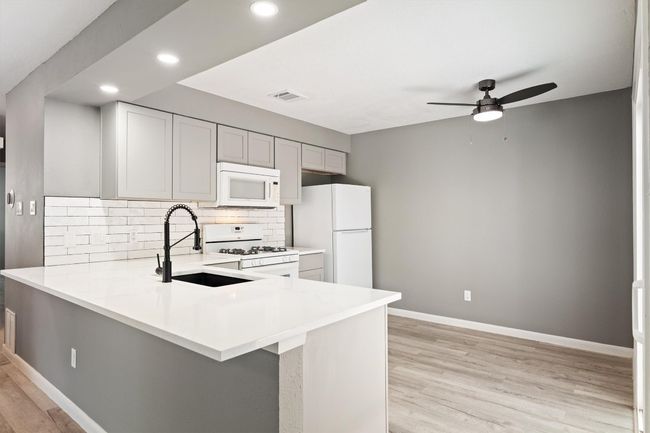 Kitchen featuring white appliances, a sink, a ceiling fan, light wood-type flooring, and light countertops | Image 15