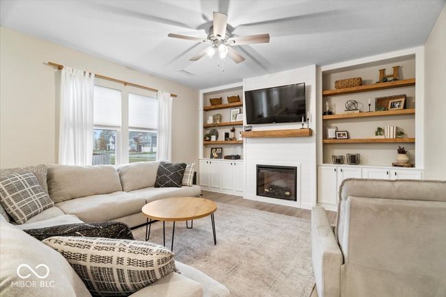 living room featuring light wood-style floors, a ceiling fan, a large fireplace, and built in shelves | Image 8
