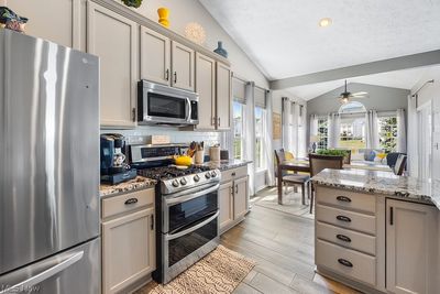 Kitchen featuring light hardwood / wood-style flooring, ceiling fan, appliances with stainless steel finishes, decorative backsplash, and vaulted ceiling | Image 3