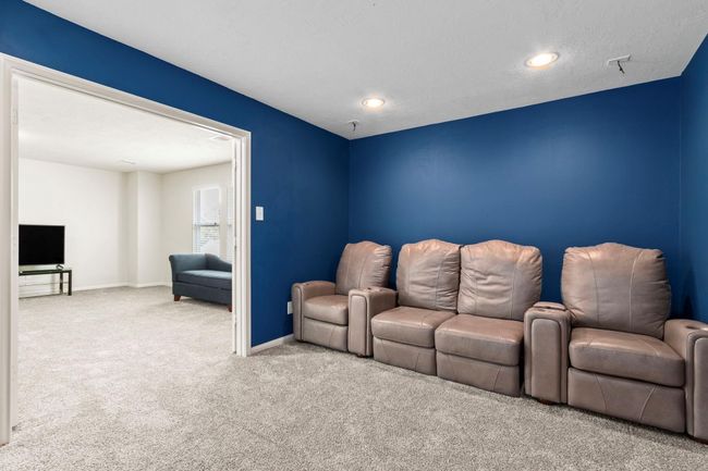 This cozy home theater features a bold blue accent wall and comfortable leather recliners, perfect for movie nights. Adjacent is a bright living space with neutral walls and carpet, offering a TV setup and additional seating. | Image 22