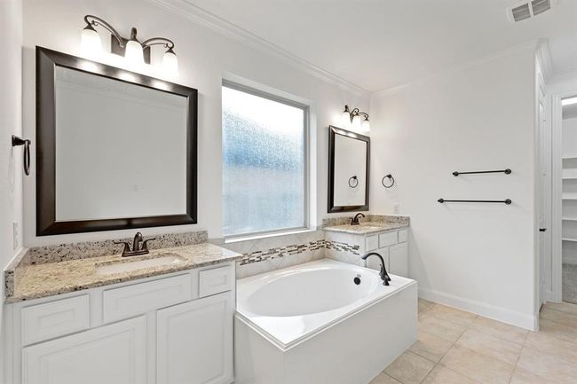 The spacious primary bathroom boasts a luxurious large bathtub, double sink vanities with ample counter space, and beautiful tile flooring, creating a perfect retreat for relaxation and convenience. | Image 11