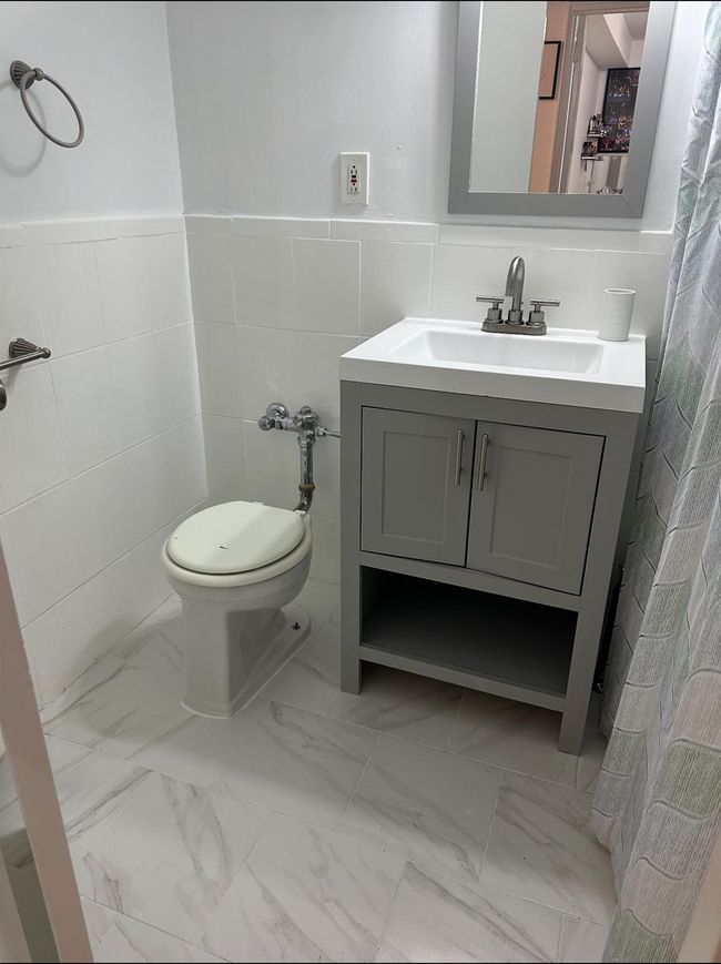 Bathroom with tile walls, marble look tile flooring, vanity, toilet, and a wainscoted wall | Image 9
