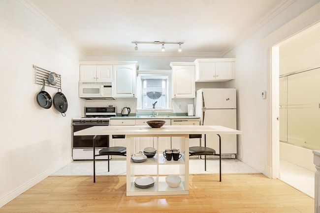 Kitchen with white appliances, white cabinetry, crown molding, light countertops, and light wood-style floors | Image 29