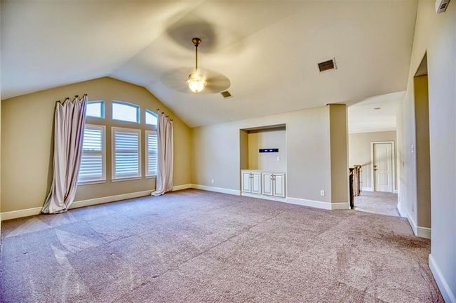 This spacious room features a vaulted ceiling, large windows with elegant drapes, and neutral carpeting. It includes a built-in cabinet and an open layout leading to a hallway, providing a versatile living space with ample natural light. | Image 39