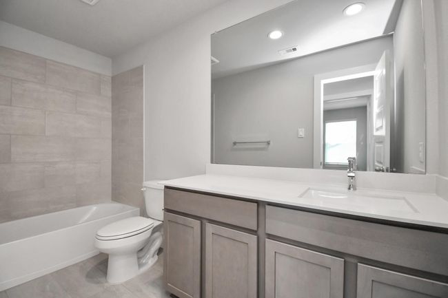 Secondary bath features tile flooring, bath/shower combo with tile surround, light stained wood cabinets, beautiful light countertop. | Image 34