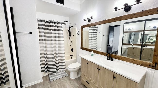Bathroom with toilet, wood finished floors, shower / tub combo with curtain, and visible vents | Image 11