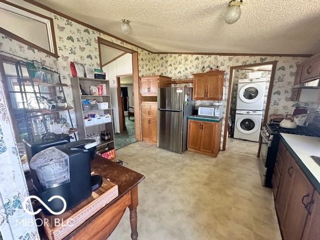 kitchen with ornamental molding, appliances with stainless steel finishes, stacked washing maching and dryer, and wallpapered walls | Image 7