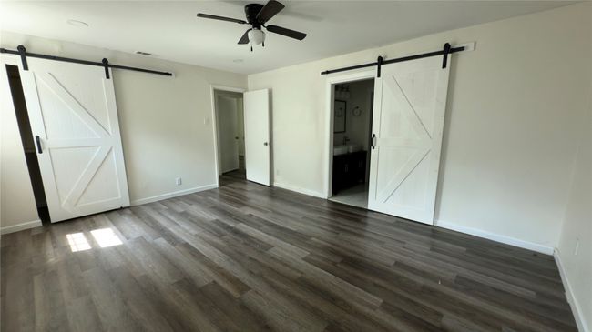 Unfurnished bedroom featuring a barn door, dark wood finished floors, connected bathroom, and a ceiling fan | Image 23