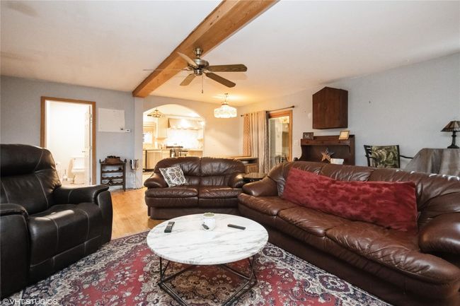 Living area with arched walkways, ceiling fan, wood finished floors, and beamed ceiling | Image 4