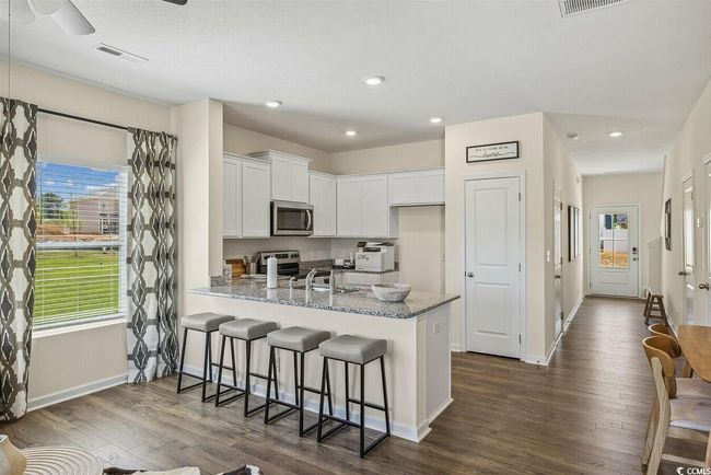 Kitchen featuring stainless steel appliances, a peninsula, white cabinets, dark wood-style flooring, and light stone counters | Image 4