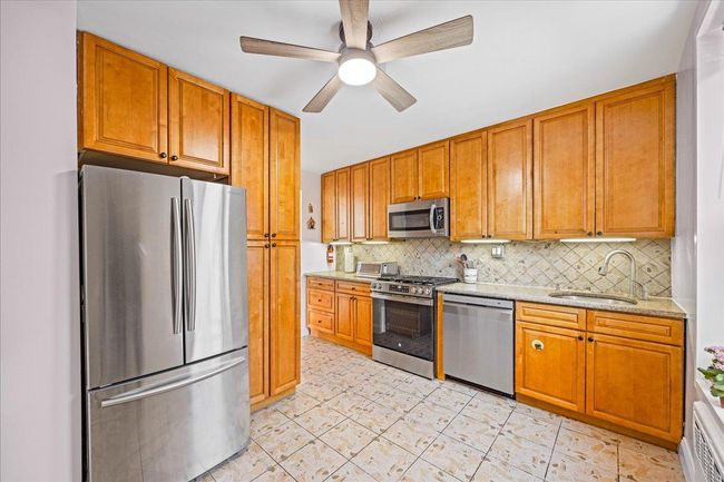 Kitchen featuring stainless steel appliances, a sink, decorative backsplash, a ceiling fan, and brown cabinets | Image 6