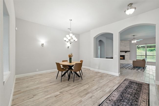 Dining area featuring light wood-type flooring, a ceiling fan, a stone fireplace, and arched walkways | Image 8