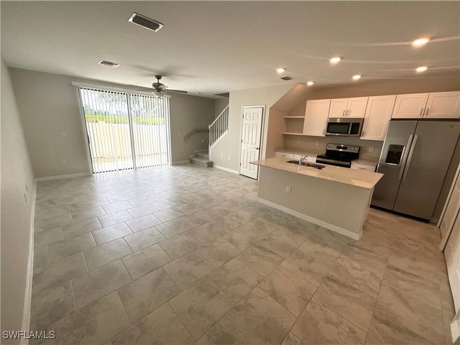 Kitchen with stainless steel appliances, light countertops, open floor plan, ceiling fan, and an island with sink | Image 5