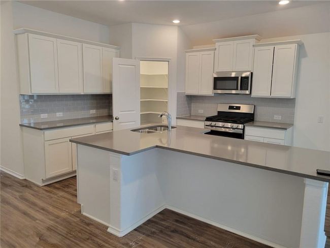 Kitchen with stainless steel appliances, recessed lighting, dark wood-type flooring, white cabinetry, and a large island | Image 5