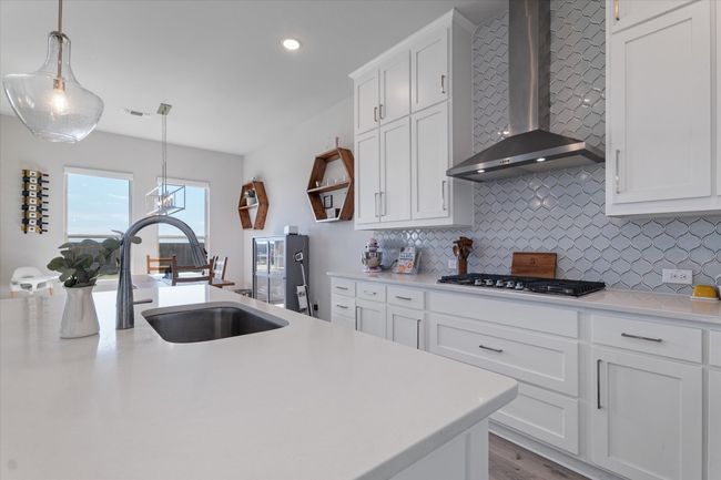 Kitchen featuring wall chimney exhaust hood, stainless steel gas cooktop, backsplash, light countertops, and recessed lighting | Image 8