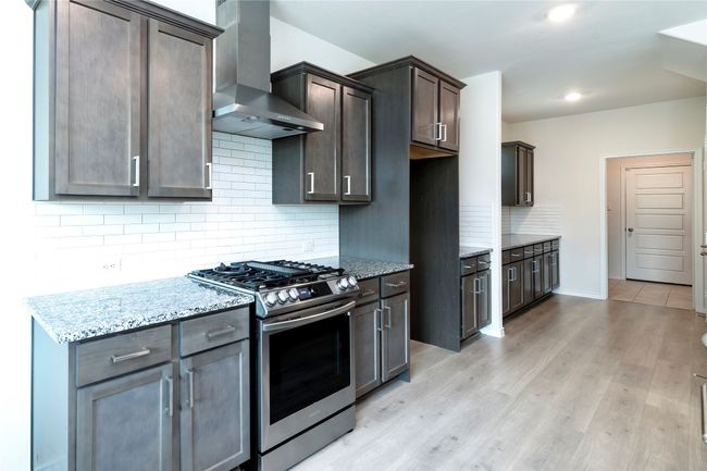 Kitchen with gas stove, backsplash, wall chimney range hood, light stone counters, and recessed lighting | Image 8