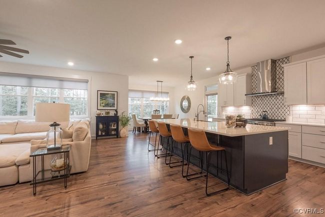 Kitchen with open floor plan, a spacious island, wall chimney exhaust hood, tasteful backsplash, and light countertops | Image 21