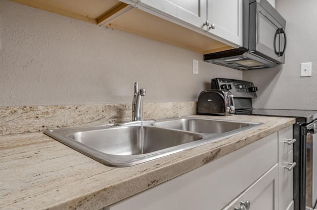 Kitchen with black range with electric cooktop, light countertops, white cabinets, and a textured wall | Image 6