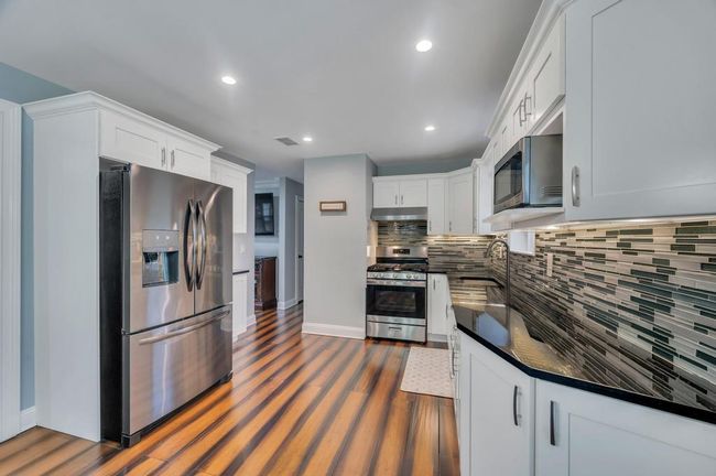 Kitchen featuring dark countertops, appliances with stainless steel finishes, dark wood-type flooring, a sink, and backsplash | Image 6