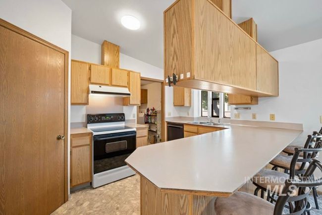 Kitchen featuring electric range oven, a kitchen bar, a peninsula, light countertops, and light brown cabinets | Image 6