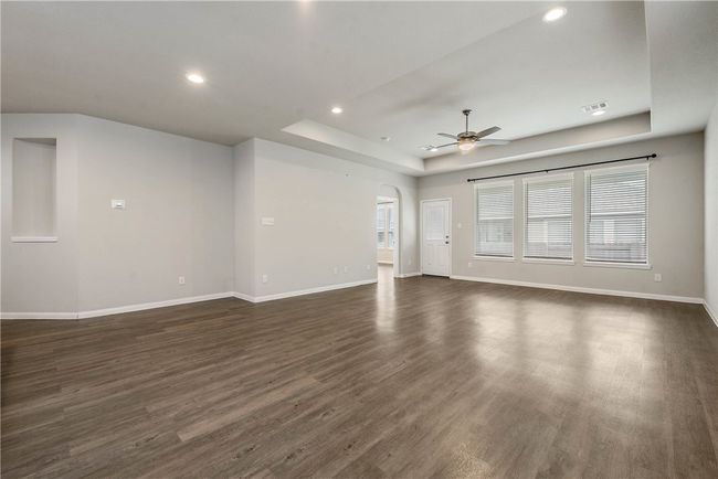 Unfurnished living room featuring a raised ceiling, a ceiling fan, dark wood-style floors, recessed lighting, and arched walkways | Image 9