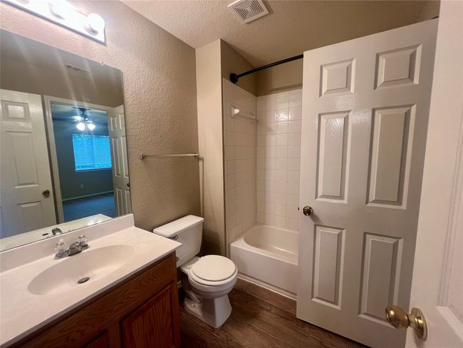 Bathroom featuring a textured wall, a textured ceiling, wood finished floors, vanity, and shower / washtub combination | Image 33