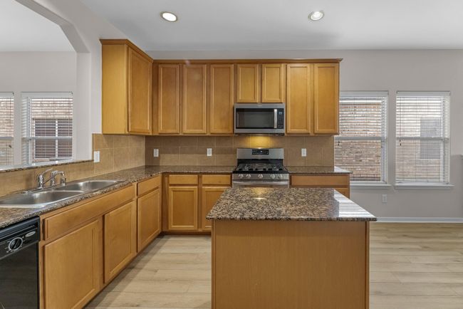 This light and bright kitchen features a granite island, wood cabinets, a large sink overlooking your family room, recessed lighting, and beautiful backsplash. | Image 9