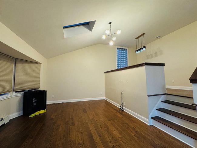 Unfurnished room featuring vaulted ceiling, wood finished floors, a skylight, a chandelier, and stairs | Image 4