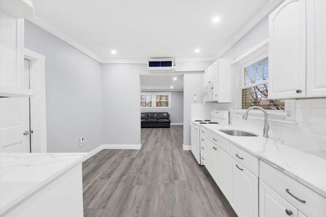 Kitchen with white appliances, a sink, healthy amount of natural light, light stone counters, and crown molding | Image 5
