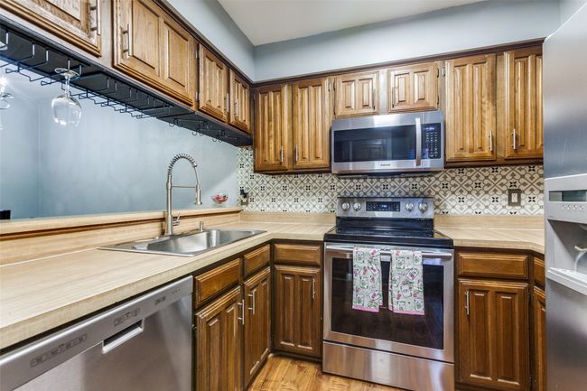 Kitchen with stainless steel appliances, light wood finished floors, decorative backsplash, and brown cabinetry | Image 11