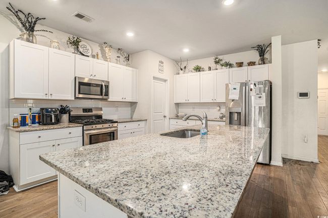 Kitchen featuring stainless steel appliances, a sink, white cabinets, hardwood / wood-style flooring, and a center island with sink | Image 12