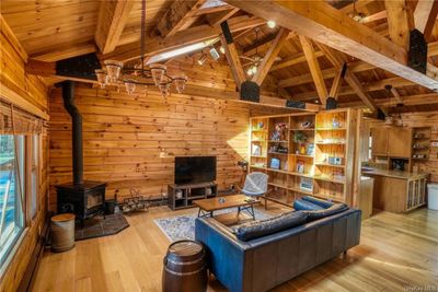 Living room with a wood stove, wooden ceiling, lofted ceiling with beams, light hardwood / wood-style floors, and wood walls | Image 1