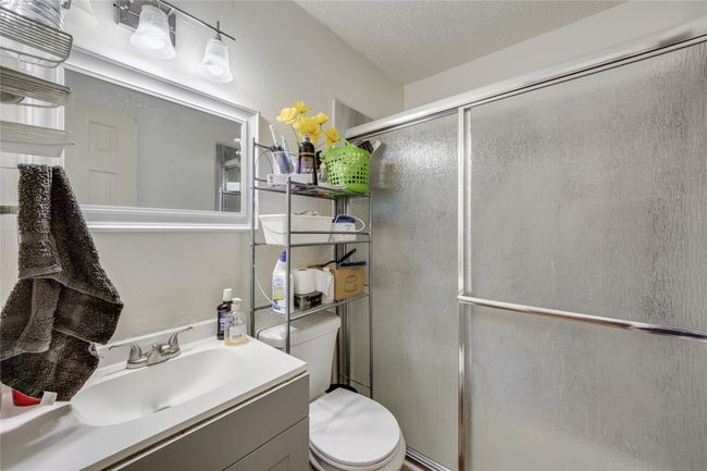 Unit A Bathroom featuring a textured ceiling, toilet, a shower with door, and vanity | Image 31