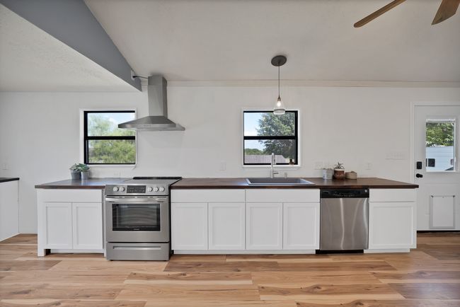 Kitchen with stainless steel appliances, wall chimney exhaust hood, a ceiling fan, white cabinets, and vaulted ceiling | Image 7