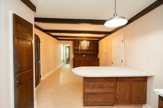 Kitchen featuring a peninsula, brown cabinetry, a chandelier, beamed ceiling, and open shelves | Image 17