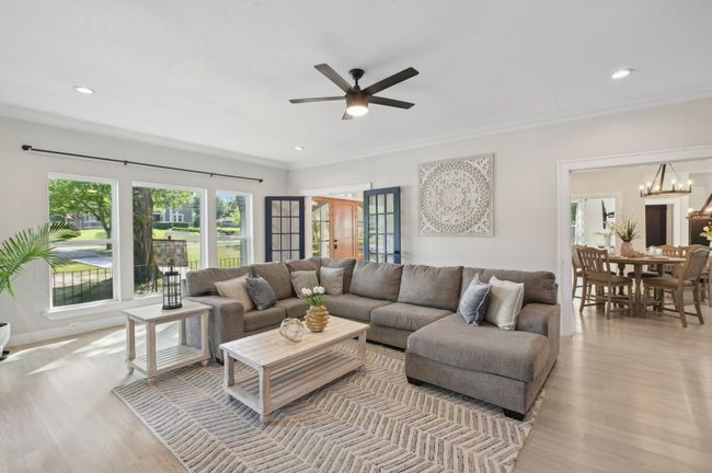 Living room with ornamental molding, light wood finished floors, a ceiling fan, a chandelier, and recessed lighting | Image 9