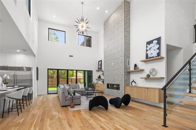 Living room with a chandelier, a large fireplace, light wood-type flooring, and a high ceiling | Image 1