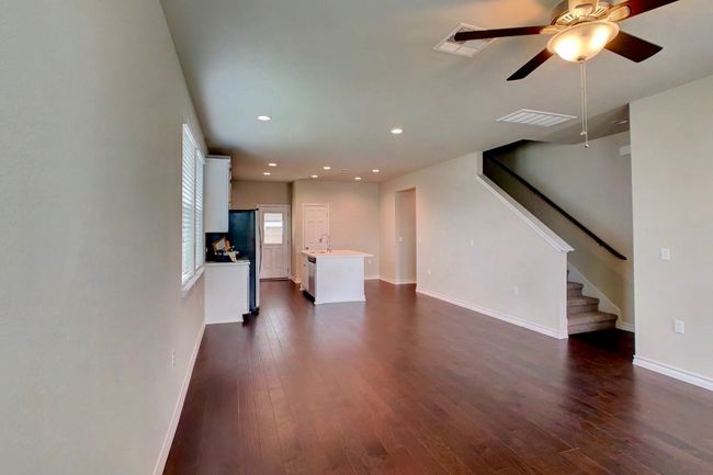 Unfurnished living room featuring stairway, dark wood-style floors, baseboards, visible vents, and ceiling fan | Image 7