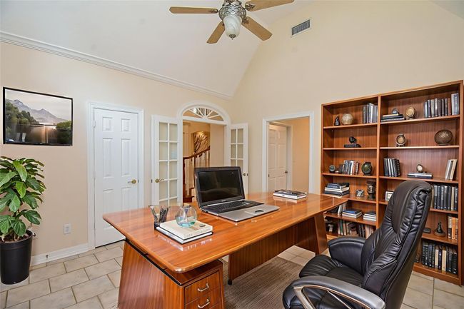 This inviting room boasts a vaulted ceiling, neutral tones, and tiled flooring. French doors open to a staircase, while additional doorways enhance accessibility. A ceiling fan adds comfort to this spacious area. *Virtually staged. | Image 13