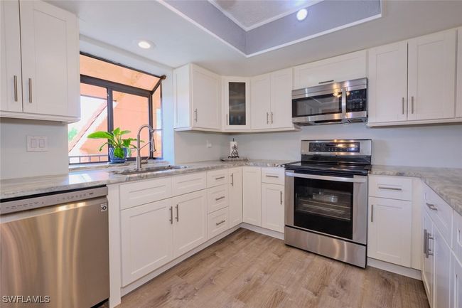 Kitchen with stainless steel appliances, white cabinetry, light wood-style flooring, a raised ceiling, and light stone counters | Image 16
