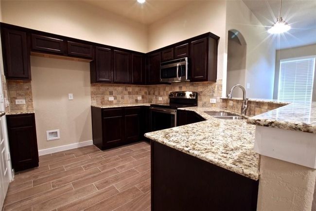 Kitchen featuring appliances with stainless steel finishes, a sink, light stone countertops, a peninsula, and backsplash | Image 7