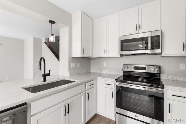 Kitchen featuring appliances with stainless steel finishes, a sink, white cabinets, light stone counters, and light wood-style floors | Image 12