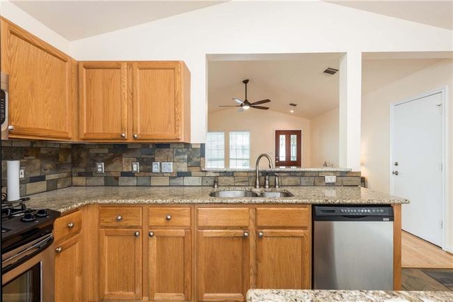 Kitchen featuring appliances with stainless steel finishes, lofted ceiling, ceiling fan, decorative backsplash, and light stone countertops | Image 13