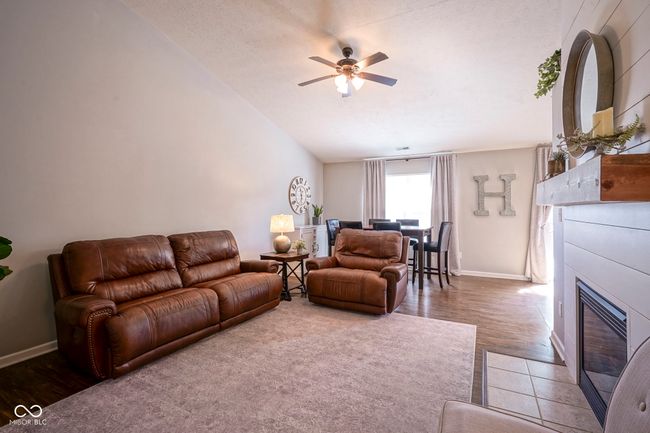 living room with baseboards, a glass covered fireplace, vaulted ceiling, wood finished floors, and a ceiling fan | Image 7