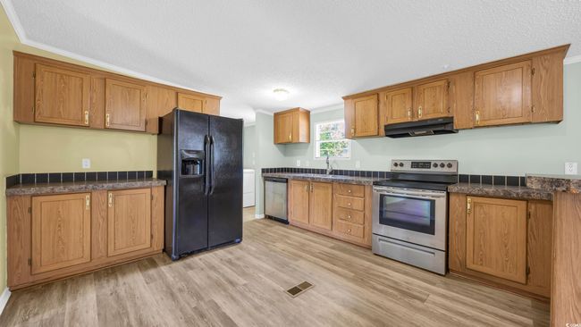 Kitchen featuring stainless steel appliances, under cabinet range hood, brown cabinets, dark countertops, and a textured ceiling | Image 7