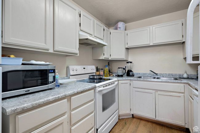Kitchen with white electric stove, stainless steel microwave, under cabinet range hood, and light countertops | Image 49