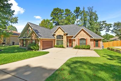 This is a one and a half-story brick home with an attached two-car garage, large windows, and a well-maintained lawn, in Elkins Lake surrounded by mature trees. | Image 2