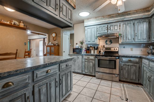 Kitchen with dark countertops, a textured ceiling, under cabinet range hood, a ceiling fan, and stainless steel appliances | Image 12