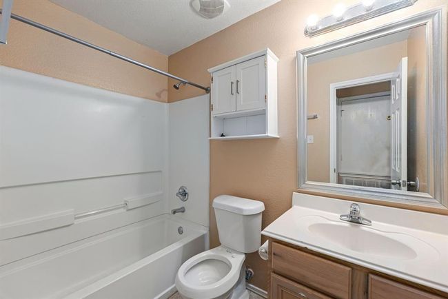 This full bathroom features a clean, classic tub/shower combo, single-sink vanity with framed mirror, and wall-mounted storage, ideal for everyday convenience. | Image 8