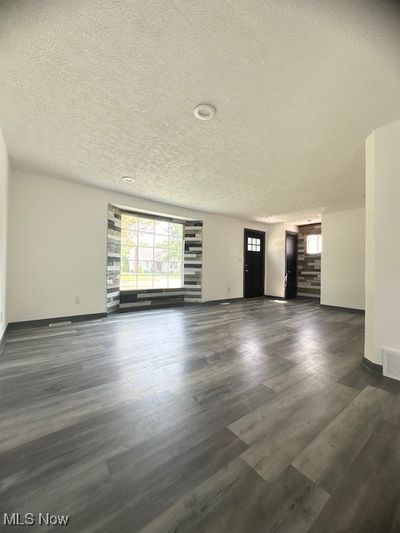 Unfurnished living room featuring dark hardwood / wood-style flooring and a textured ceiling | Image 3